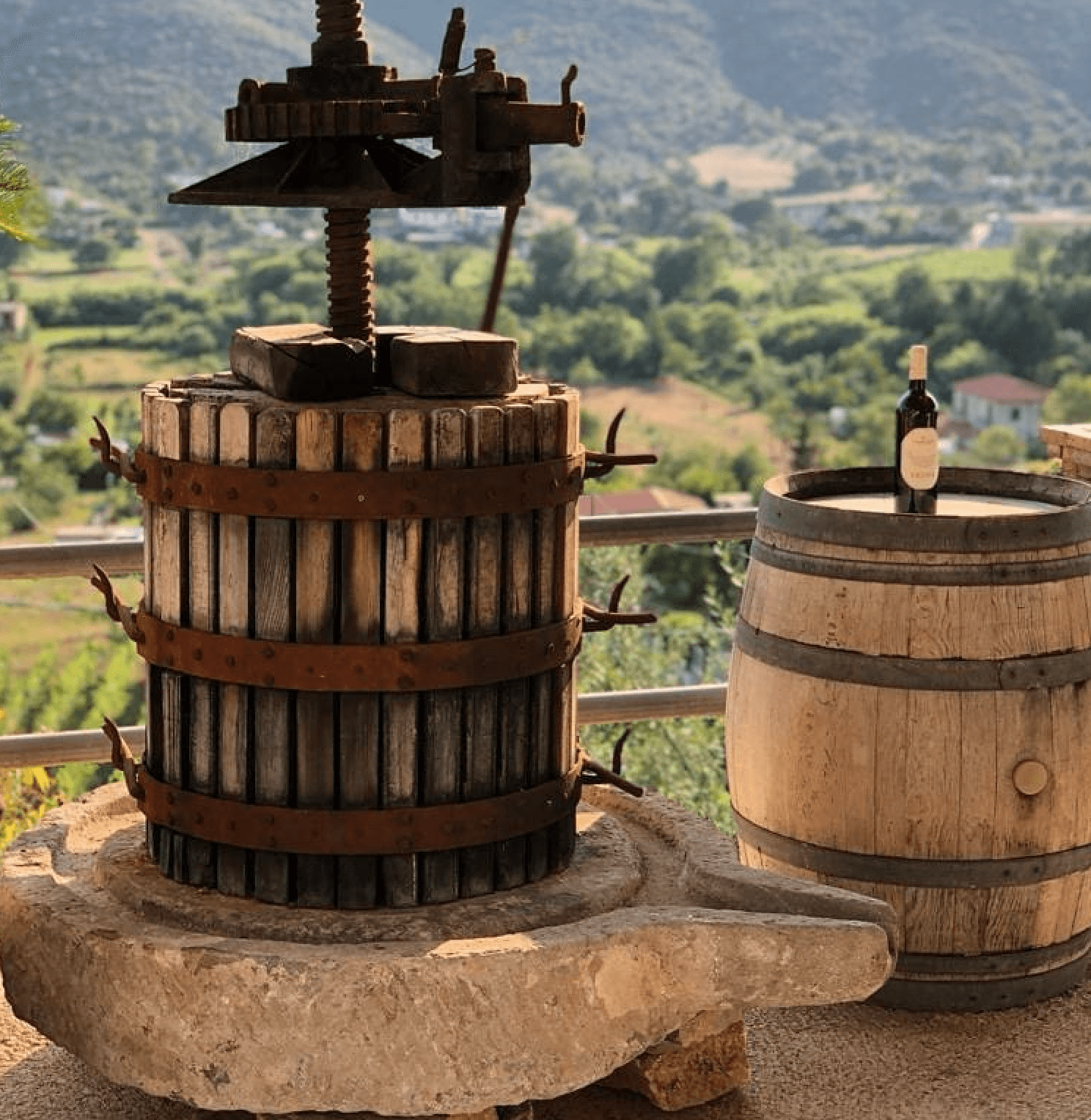 Rustic wine press and barrel overlooking a scenic valley.